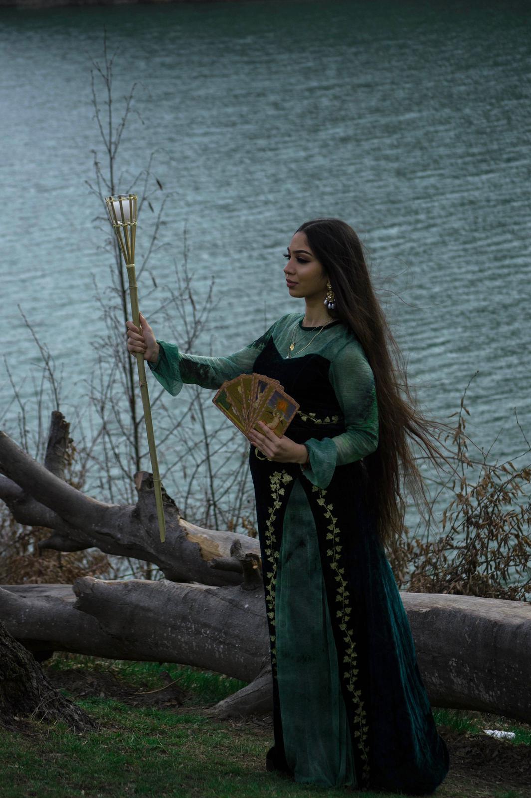 Tămăduitoarea Malvina Diana, în rochie de catifea verde, la malul apei, ținând făclia și cărțile de tarot